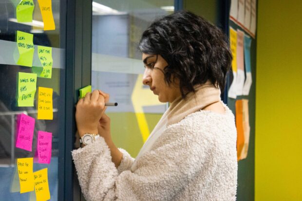 A photo of person writing sticky notes and adding them to an office wall.